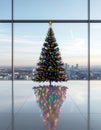festive Christmas tree adorned with colorful lights stands in front of large windows overlooking a city skyline. Royalty Free Stock Photo