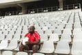 Upset African American male rugby player sitting with rugby ball in stadium