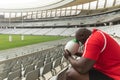 Upset African American male rugby player sitting with rugby ball in stadium Royalty Free Stock Photo