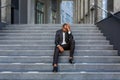 Upset african american man sitting on stairs outside office building, businessman bankrupt in despair, mature boss Royalty Free Stock Photo