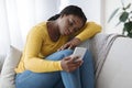 Upset African Woman Sitting On Couch With Smartphone, Feeling Lonely And Depressed Royalty Free Stock Photo