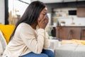 Upset african-american woman sitting on the sofa in grief, closing eyes with palms Royalty Free Stock Photo