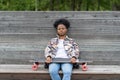 Upset african woman tired or depressed sit in apathy on bench with longboard in urban space alone