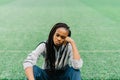 The upset afro-american teenager is sitting on the grass and leaning on her hand.