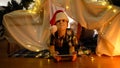 Displeased little boy in Santa hat lying in tent using phone. Christmas concept.