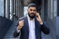 Upset and angry Indian male businessman standing outside an office center and talking on the phone emotionally Royalty Free Stock Photo