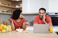 Upset angry millennial black female swears at man, speaks on phone with laptop in kitchen interior Royalty Free Stock Photo