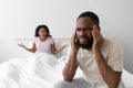 Upset angry young african american wife yelling at sad unhappy husband on white bed in bedroom interior Royalty Free Stock Photo