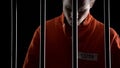 Upset arrested man in orange suit behind prison bars, death penalty judgment