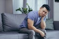 Upset Asian man at home, tired and depressed sitting on the couch in the living room Royalty Free Stock Photo