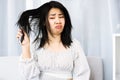 Upset Asian woman using comp brushing her dry ,damaged hair unhappy with messy hair