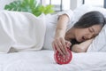 Upset asian young woman displeased stopping ringing red alarm clock on white bed in morning. Angry unhappy young girl sleeping Royalty Free Stock Photo