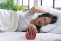 Upset asian young woman displeased stopping ringing red alarm clock on white bed in morning. Angry unhappy young girl sleeping Royalty Free Stock Photo