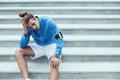 Athlete after failure workout sitting on the stairs on the street and holding his head, armband with mobile phone and
