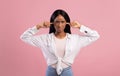 Upset black lady closing her ears with fingers, protecting from loud noise on pink studio background Royalty Free Stock Photo