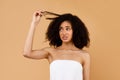 Upset black lady touching her curly hair, worried about dry edges of damaged bushy hair, posing on beige background Royalty Free Stock Photo