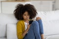 Upset black teen girl sitting on sofa, using smartphone Royalty Free Stock Photo