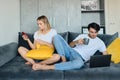 Upset blond woman with glass of orange juice in hand using cellphone while thoughtful brunette man with cup of coffee Royalty Free Stock Photo