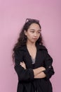 An upset and bored asian woman with arms crossed. Wearing a black trench coat against a light pink background Royalty Free Stock Photo