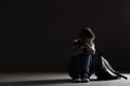 Upset boy with backpack sitting in dark room