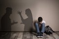 Upset boy sitting on floor and silhouettes of arguing parents