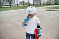 Upset boy skateboarder in protective gear frustratedly wipes tears from his eyes and holds a skateboard in one hand while standing Royalty Free Stock Photo