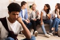 Upset bullied guy sitting alone, excluded by bad friends