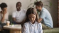 Upset bullied young girl sitting alone excluded by bad friends