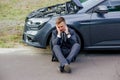 Upset businessman use phone sitting on road near the broken car opened the hood help repair Royalty Free Stock Photo