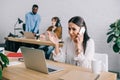 upset businesswoman talking on smartphone and colleagues working behind in modern