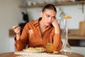 Upset caucasian woman eating tasteless pasta or needs to keep diet, sitting at table in kitchen interior Royalty Free Stock Photo