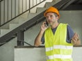 Upset construction worker or stressed contractor man in hardhat and vest talking on mobile phone unhappy in stress messing with