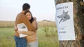 Upset couple hugs in park focus on poster of missing cat