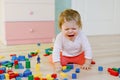 Upset crying baby girl with educational toys. Sad tired or hungry alone healthy child sitting near colorful different