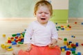 Upset crying baby girl with educational toys. Sad tired or hungry alone healthy child sitting near colorful different