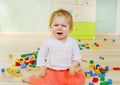 Upset crying baby girl with educational toys. Sad tired or hungry alone healthy child sitting near colorful different