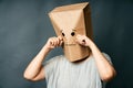 Upset crying woman with a paper bag on head over gray background