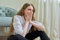 Upset crying young woman sitting at home on the floor.