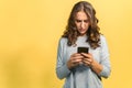 Upset attractive woman with a smartphone, isolated on yellow