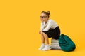 Upset Cute Schoolgirl Sitting On Pile Of Books Over Yellow Studio Background Royalty Free Stock Photo