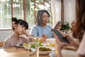 Upset daughter sitting at lunch table looking to addicted parents and grandparents using smartphones while eating breakfast. Ignor