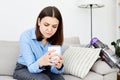 Upset depressed brunette lady wearing blue shirt touching head, sitting on sofa, looking down, feeling worried and stressed about Royalty Free Stock Photo