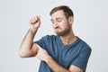 Upset dissatisfied bearded guy wearing blue t-shirt posing at studio tensing muscles to show his biceps, curving lips Royalty Free Stock Photo