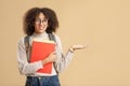 Upset doubt african american woman in glasses with backpack holds notepads and shows hand to blank space Royalty Free Stock Photo