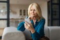 Upset european mature woman sitting on couch at home, holding cell phone, looking at gadget screen, reading bad news Royalty Free Stock Photo