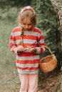 Upset or focused eight year old kid girl mushroom picker is seek for and picking mushrooms in the forest or woodland. child surviv