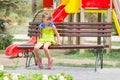 Upset girl bit her lip while sitting on bench on the background of the playground Royalty Free Stock Photo