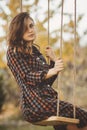 Upset girl in a dress sways on swing in the autumn garden, a young woman in melancholy mood thinkng on nature