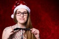 Upset girl with glasses in a santa hat on a red background Royalty Free Stock Photo