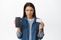 Upset gloomy woman showing mobile phone screen, empty display on smartphone and credit card, furrow eyebrows Royalty Free Stock Photo